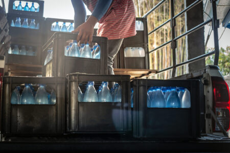 Getränkelieferung: Person lädt Wasserkästen mit Flaschen aus dem Lieferfahrzeug – Heimzustellung/Lieferdienst für Getränke.