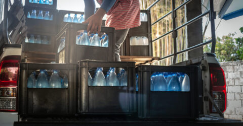 Getränkelieferung: Person lädt Wasserkästen mit Flaschen aus dem Lieferfahrzeug – Heimzustellung/Lieferdienst für Getränke.