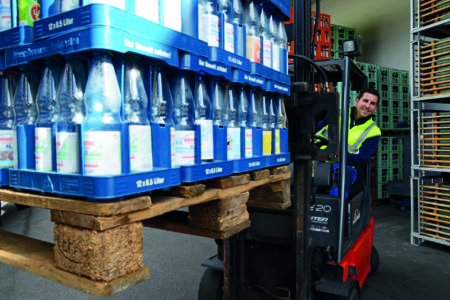 Mitarbeiter fährt mit einem Gabelstapler im Getränkelager und transportiert Paletten mit Getränkekisten und Glasflaschen.
