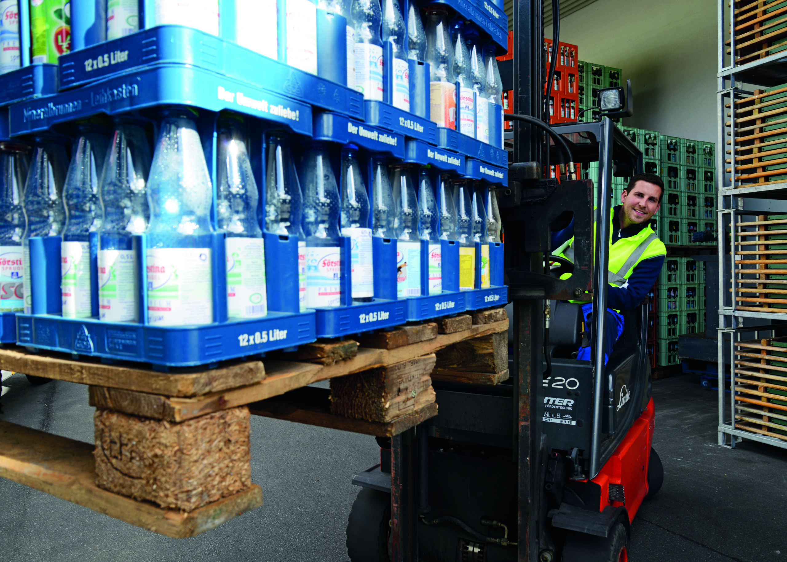 Mitarbeiter fährt mit einem Gabelstapler im Getränkelager und transportiert Paletten mit Getränkekisten und Glasflaschen.