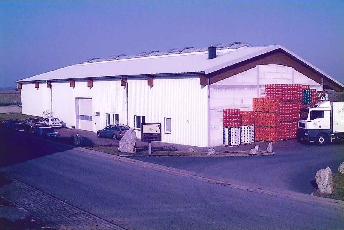 Neubau der Lagerhalle im Gewerbegebiet ‚Am Grund‘ (1997–1998) mit gestapelten Getränkekisten und LKW vor dem Gebäude.